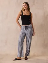 Pantalón largo de lino y rayón a rayas verticales grises y blancas. Tiene pretina elastizada con lazo de ajuste, bolsillos delanteros y traseros.