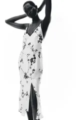 Vestido largo blanco con estampado de flores negras, escote pico y tirantes finos con ribete negro.