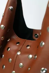 Cartera tipo hobo de cuero color marrón con apliques de tachas plateadas.