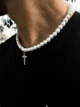 Collar de perlas blancas con dije de cruz plateada con incrustaciones de strass.