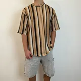 Remera tejida de punto con rayas verticales en tonos beige, marrón y negro, de corte oversize y mangas cortas.