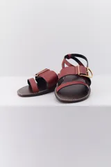 Sandalia plana de cuero en tonos marrón y negro, con detalle de hebilla en el tobillo y diseño minimalista.