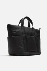 Bolso tipo shopper negro fabricado en tejido técnico. Cuenta con un compartimento principal con cierre de cremallera y un bolsillo interior con cierre. En la parte frontal tiene tres bolsillos. Tiene dos asas de mano.