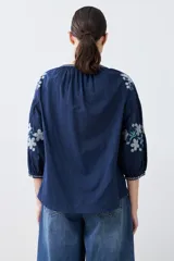 Blusa blanca de estilo boho con bordados de flores en amarillo y azul en mangas y escote.