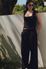 Pantalón negro con bordados florales en los laterales, tiro alto, cintura elástica en la parte trasera, bolsillos laterales, pliegues y cierre frontal con cremallera, botón interior y gancho metálico.