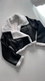Campera corta negra de cuero sintético con interior y cuello de piel sintética blanca.