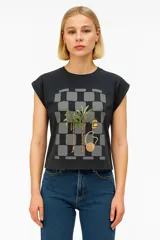 Remera negra de algodón con estampado de palmeras, botella de aceite de coco y bolso de playa sobre un fondo a cuadros grises.