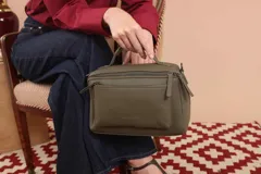 Bandolera color marrón con asa superior y correa larga ajustable. Tiene dos bolsillos frontales, uno de ellos con cierre cruzado.