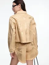 Campera corta de denim color rojo con textura metalizada, cuello camisero, cierre frontal con botones a presión, bolsillos de parche en el pecho y ruedo desflecado.