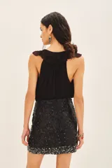 Falda corta negra de tiro medio, confeccionada en viscosa crepe, con bordado de lentejuelas y piedras en tonos plateados y blancos, concentrados principalmente en el ruedo.
