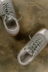 Zapatilla plateada de cuero con detalles de gamuza gris y costuras visibles.