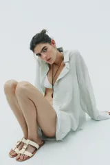 Sandalia plana color crema con doble tira y hebilla metálica dorada.