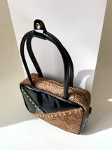 Cartera rígida negra de cuero con tachas plateadas y tres combinaciones de cuero diferentes que aportan textura. Tiene herrajes y cierre metálico plateado marca YKK. Cuenta con un asa fina para llevar al hombro o en la mano y una correa larga extra regulable.