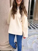 Canguro de paño color crema, de corte holgado y cuello redondo, con puños y ruedo acanalados.