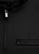 Chaqueta corta negra con cuello mao, cierre frontal con cremallera, dos bolsillos laterales y un bolsillo de ribete en el pecho.