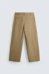 Pantalón color beige de corte ancho, con pliegues frontales dobles, bolsillos laterales y traseros de vivo. Largo cropped y cierre frontal con cremallera y botón.
