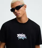 Remera negra de algodón con cuello redondo y mangas cortas. Presenta un estampado frontal con la frase "Divine Spark" y un estampado grande en la espalda de un ángel con halo y rayos celestes.