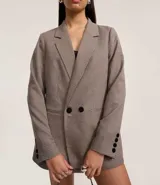 Blazer de sastre alargado, cruzado con doble botón, de manga larga y cuello solapa. Presenta un estampado de cuadros pata de gallo (pied de poule) en tonos marrones y beige.
