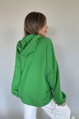 Canguro verde con capucha y cordones blancos, de corte oversize y mangas largas con puños elásticos.