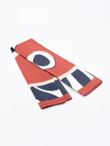 Pañuelo rectangular con estampado abstracto en tonos terracota, negro, blanco y beige.