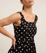 Vestido midi evasê negro con lunares blancos, breteles anchos, escote cuadrado y lastex en la espalda.