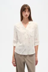 Blusa de manga tres cuartos color crema con estampado floral en azul. Presenta cuello mao con abertura en V y un bolsillo de parche en el pecho.