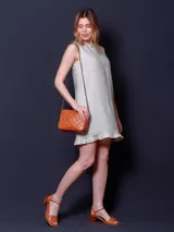 Vestido corto sin mangas, color beige claro, con cuello redondo y un pequeño volante en el ruedo.