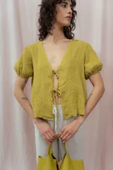 Blusa blanca de lino con escote en V, mangas cortas abullonadas y cierre frontal con lazos.