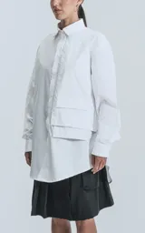 Camisa blanca de manga larga, confeccionada en poplín de algodón, con calce oversize y un bolsillo frontal asimétrico y poco convencional.