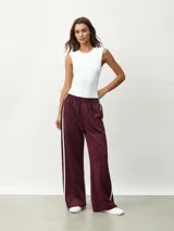 Pantalón deportivo color borgoña, de corte ancho y cintura elástica. Presenta una franja blanca vertical a lo largo de la pierna.