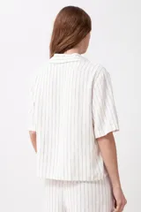 Blusa de lino a rayas verticales blancas y negras, con cuello camisero y mangas cortas.
