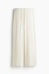 Pantalón de pijama color blanco roto, confeccionado en tejido pointelle suave. Presenta piernas levemente acampanadas, elástico revestido en la cintura con cordón fino para ajustar y ribete de volados.