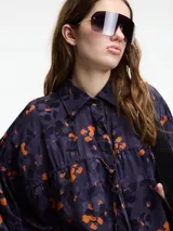 Camisa de viscosa estampada con flores color naranja sobre fondo azul marino. Tiene botones en la parte delantera y lazo ajustable.