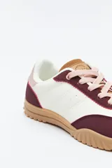 Zapatilla urbana de mujer con silueta retro, combinando paneles de gamuza marrón oscuro y material color crema en el cuerpo. Presenta detalles en color bordó en el talón y cordones beige. La suela es robusta de color marrón claro con relieve.