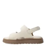Sandalia beige con ajuste de velcro y suela marrón.