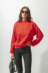 Buzo rojo de corte holgado con cuello redondo y mangas largas. Presenta una costura horizontal en el pecho y bordado con el nombre de la marca.