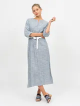 Túnica midi de lino color crudo/beige, con patrón de rayas finas verticales en tonos claros (posiblemente blanco y rosado/naranja muy sutil). Presenta cuello en V con abertura y mangas 3/4.