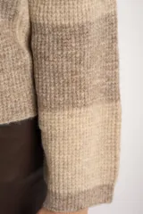 Sweater de tejido de punto grueso, con diseño de rayas verticales anchas en tonos marrón oscuro y negro. Presenta cuello redondo y mangas largas.