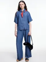 Camisa negra de manga corta confeccionada en denim liviano de tencel, de calce cuadrado y relajado. Presenta cierre frontal con tapeta escondida y costuras en color contraste.