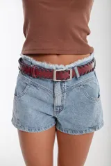 Cinturón de cuero color bordó con costura de tientos en color azul oscuro a lo largo de los bordes. Posee hebilla metálica rectangular plateada.