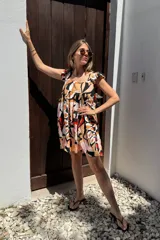 Vestido corto con estampado abstracto en tonos rosa, beige, negro y rojo. Tiene escote cuadrado, breteles anchos con volados y corte holgado.