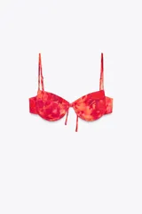 Top de bikini con estampado tie-dye en tonos rojo y naranja. Tiene aros, escote corazón, tirantes finos ajustables y cierre trasero con lazo.