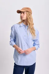 Camisa celeste con rayas verticales blancas, de corte holgado, manga larga y cuello clásico.