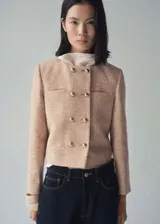 Chaqueta corta de tweed color rosa pálido con doble botonadura dorada, cuello redondo y bolsillos de parche en el pecho.