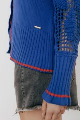 Cárdigan azul con detalles en crochet, mangas con volado y vivos de color rojo en cuello, puños y frente. Tiene botones al frente.