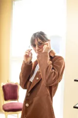 Blazer de cuero gamuza color marrón, con solapas y un botón frontal blanco. La prenda está decorada con varios pines metálicos y uno de ónix negro en la solapa izquierda.