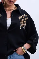 Camisa negra de mangas largas con puños abotonados y bordados dorados en el frente.