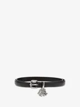 Cinturón delgado de cuero negro con hebilla metálica plateada y un dije colgante de metal plateado con incrustaciones de cristales que forman letras.