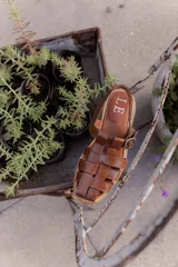 Sandalias de cuero marrón con tiras entrecruzadas y hebilla dorada al tobillo.