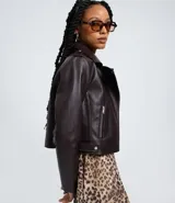 Campera biker marrón de cuero sintético con cuello con solapa, cierre frontal asimétrico con cremallera, bolsillos con cremallera y tiras con botones en los laterales.